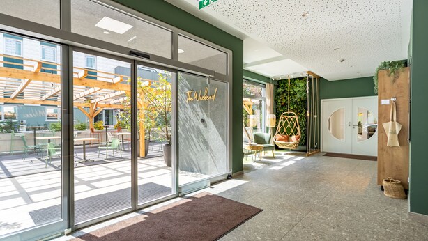 Um lobby de hotel moderno com grandes portas de vidro, balcão de recepção e vista para a área externa com varanda.