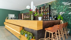 Uma área de recepção com balcão de madeira, banquetas e uma parede verde com um mural de folhas.