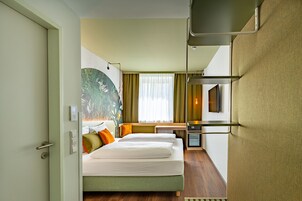 Quarto de hotel com cama, mesa de cabeceira e televisão.