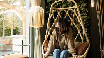 Relax in a serene space with a wicker swing chair, large window, and lush green garden wall.