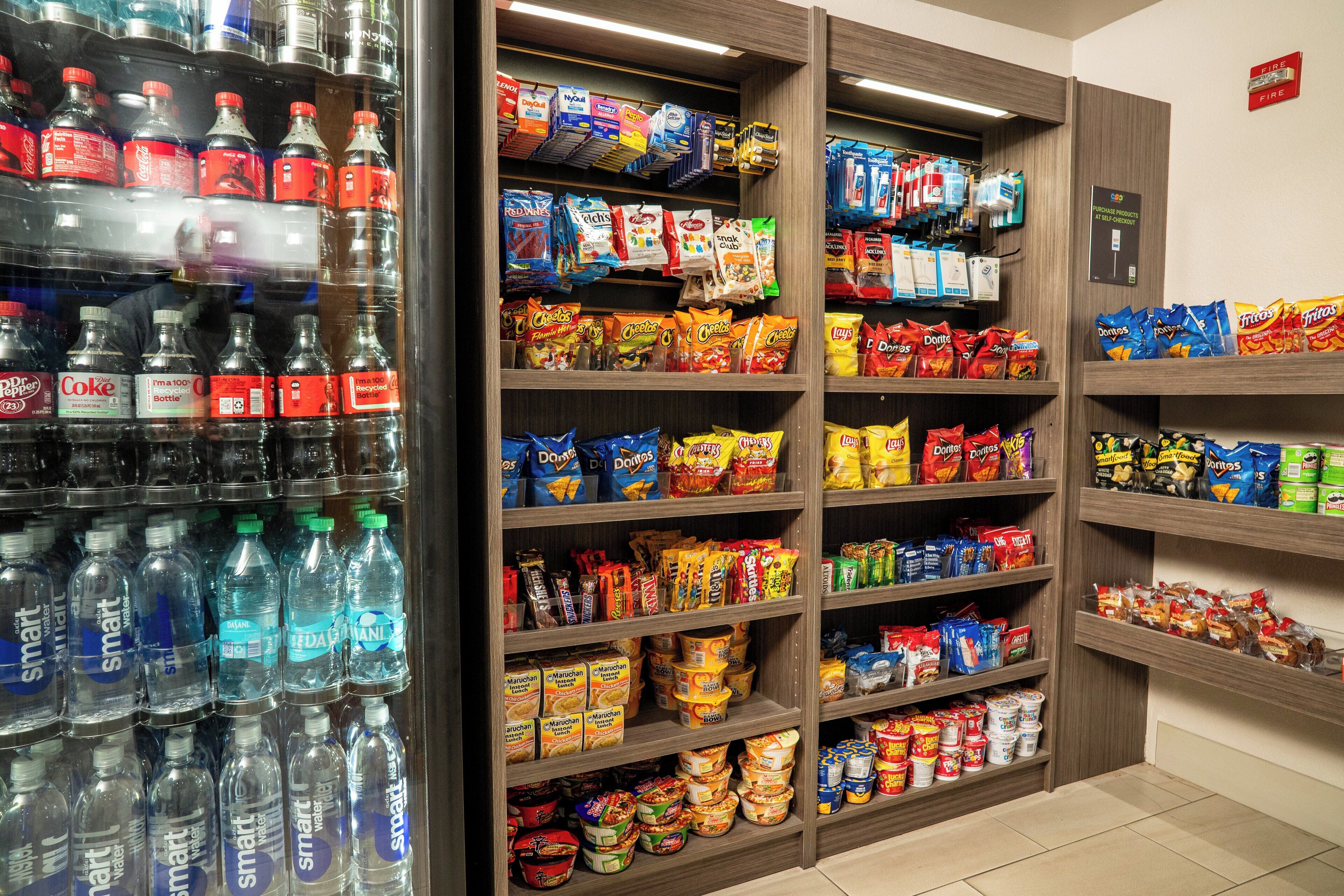 Un espacio autoservicio con bebidas y aperitivos, que incluye varias aguas embotelladas, refrescos y paquetes de snacks.