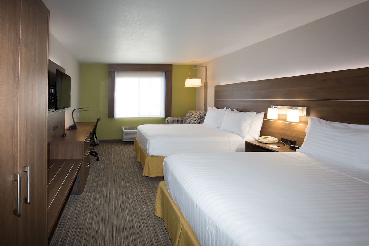 A hotel room with two beds, a television, a desk, and a window.
