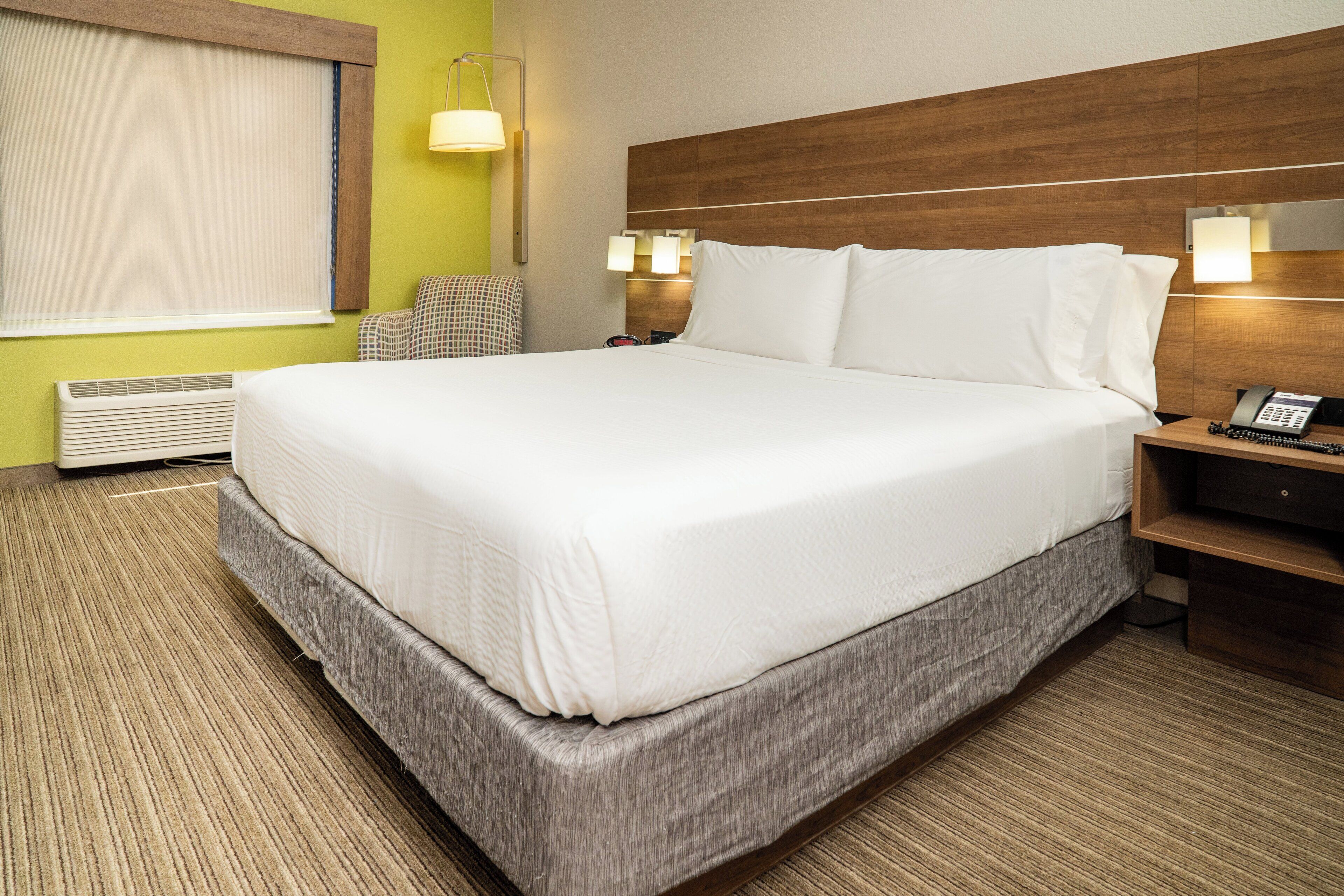 A hotel room with a large bed, a bedside table with a lamp, a chair, and a wall-mounted phone.