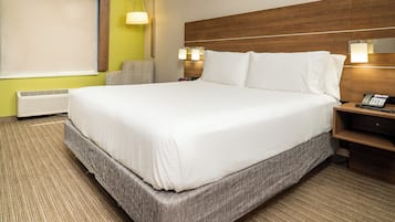 A hotel room with a large bed, a bedside table with a lamp, a chair, and a wall-mounted phone.