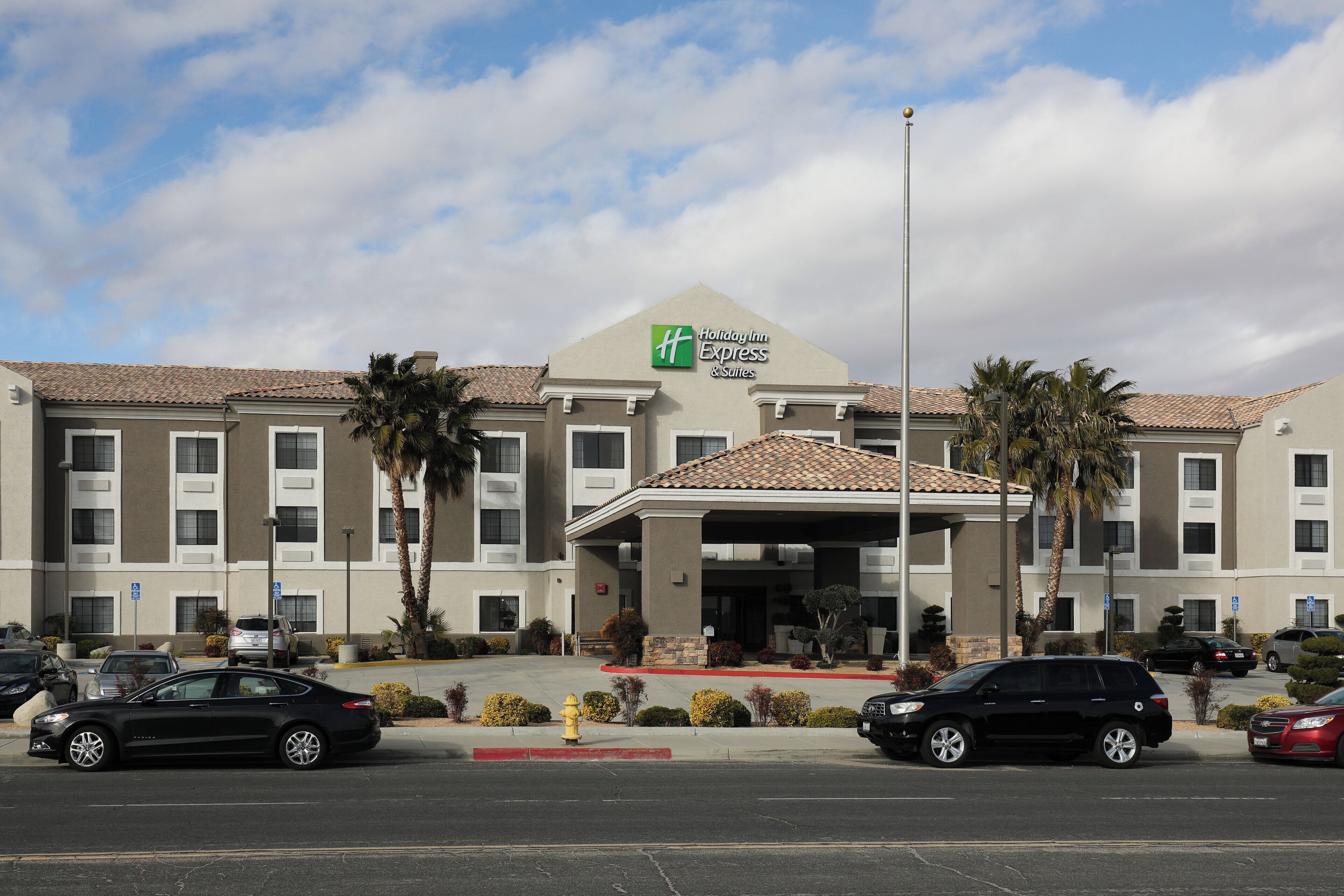 Et Holiday Inn Express & Suites hotel med overdækket indgang, flere etager og en parkeringsplads med biler.
