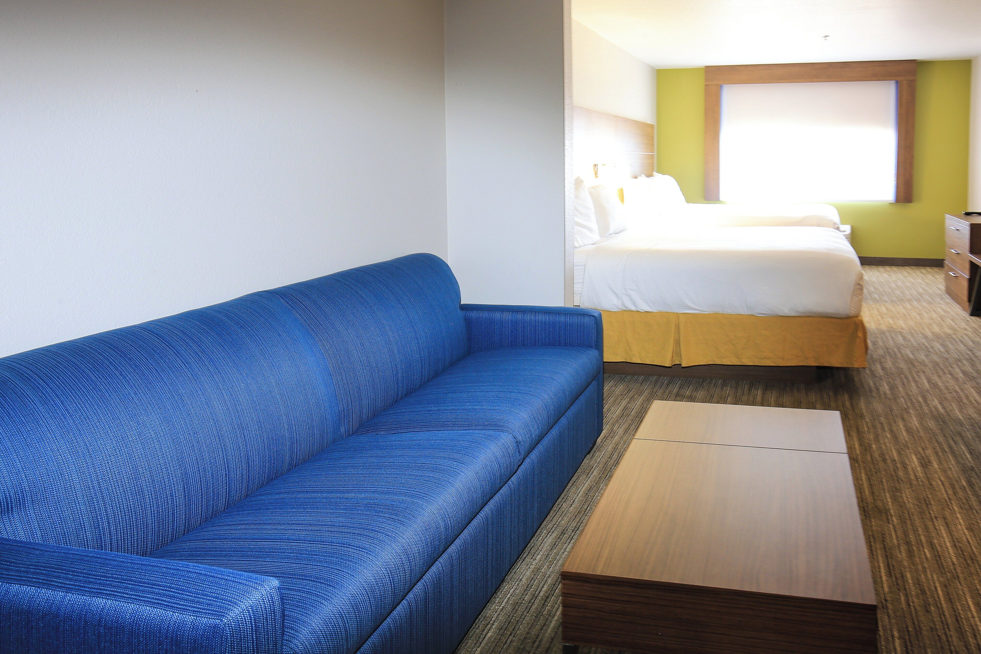 A hotel room with a blue sofa, a wooden nightstand, a bed with white bedding, and a green accent wall.