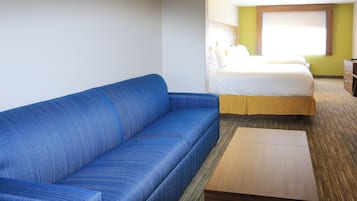 A hotel room with a blue sofa, a wooden nightstand, a bed with white bedding, and a green accent wall.