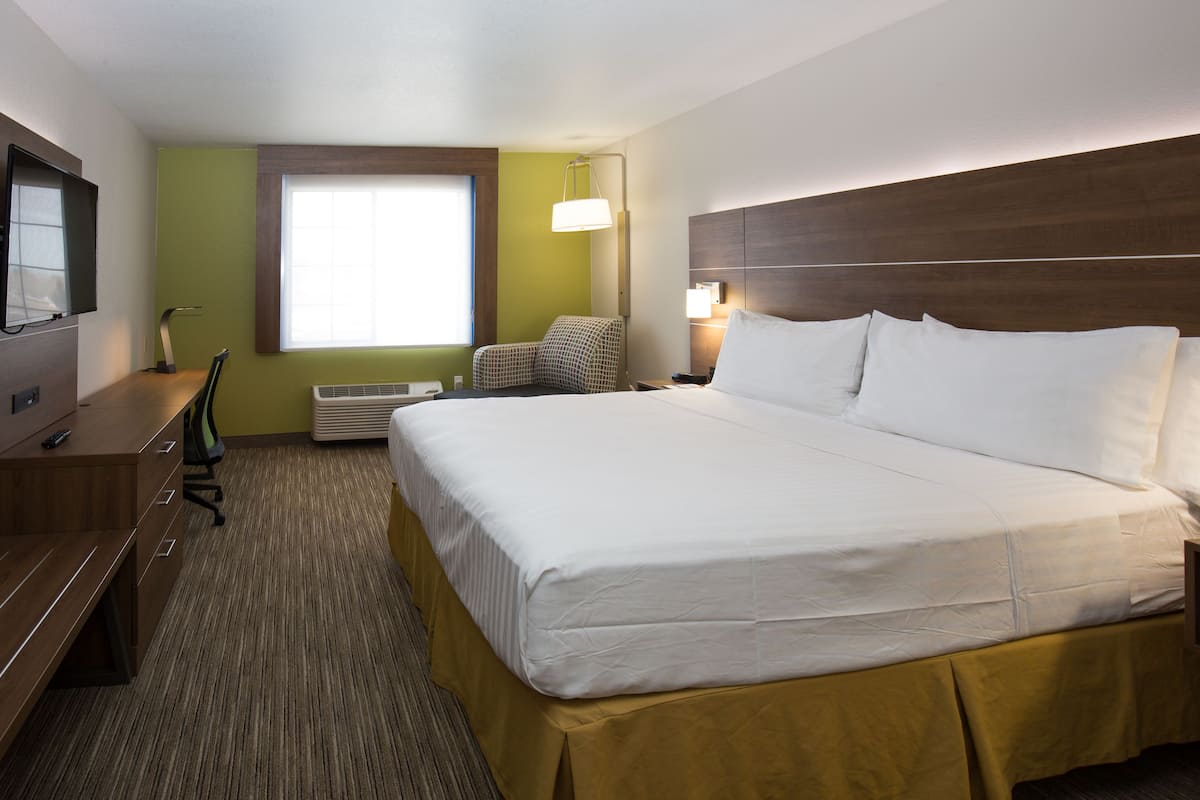 A hotel room with a large bed, a desk with a chair, a television, and a window with blinds.