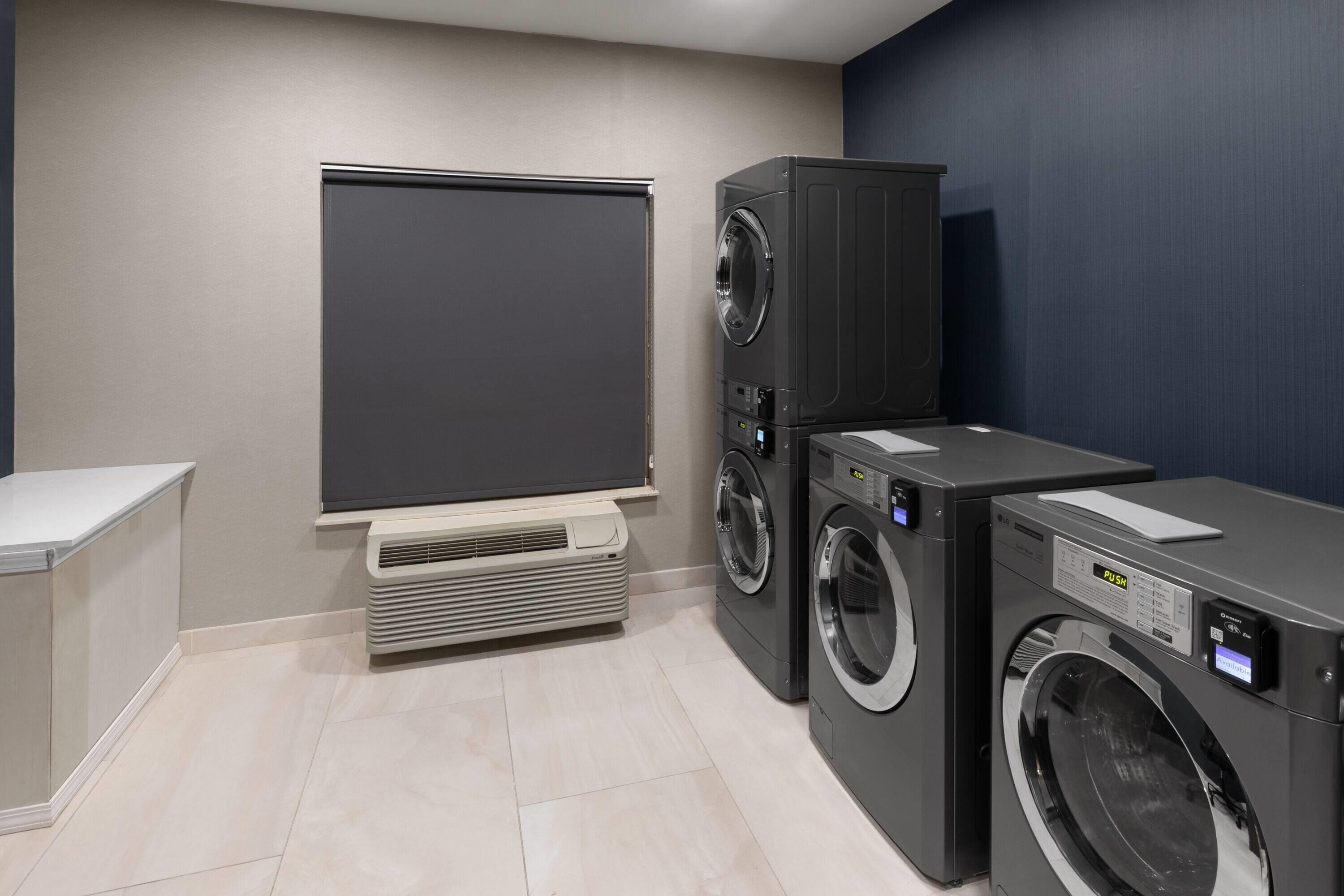 A laundry room with a wall-mounted dryer, a stacked washer and dryer unit, and a built-in air conditioning unit.