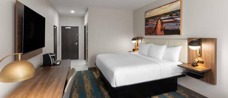 Une chambre d’hôtel équipée d’un lit, d’un bureau, d’une chaise, d’une télévision et d’œuvres d’art accrochées au mur.