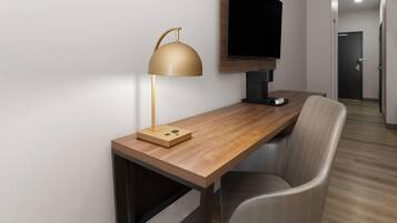 A hotel room with a wooden desk, a modern lamp, a flat-screen TV, and a chair.