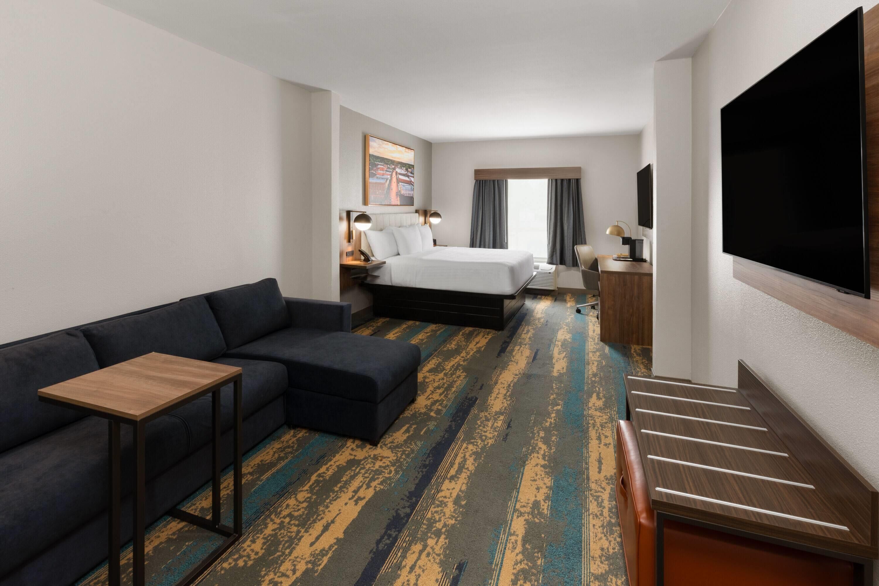 A hotel room with a bed, a sofa, a TV, a desk, and a staircase.