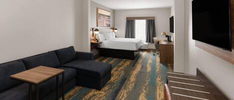 A hotel room with a bed, a sofa, a TV, a desk, and a staircase.