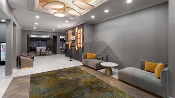 A modern hotel lobby with a grey sofa, a round coffee table, a patterned rug, and a unique ceiling light fixture.