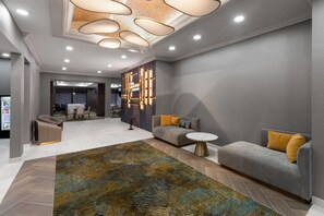 A modern hotel lobby with a grey sofa, a round coffee table, a patterned rug, and a unique ceiling light fixture. - La Quinta Inn & Suites Nacogdoches (Nacogdoches)