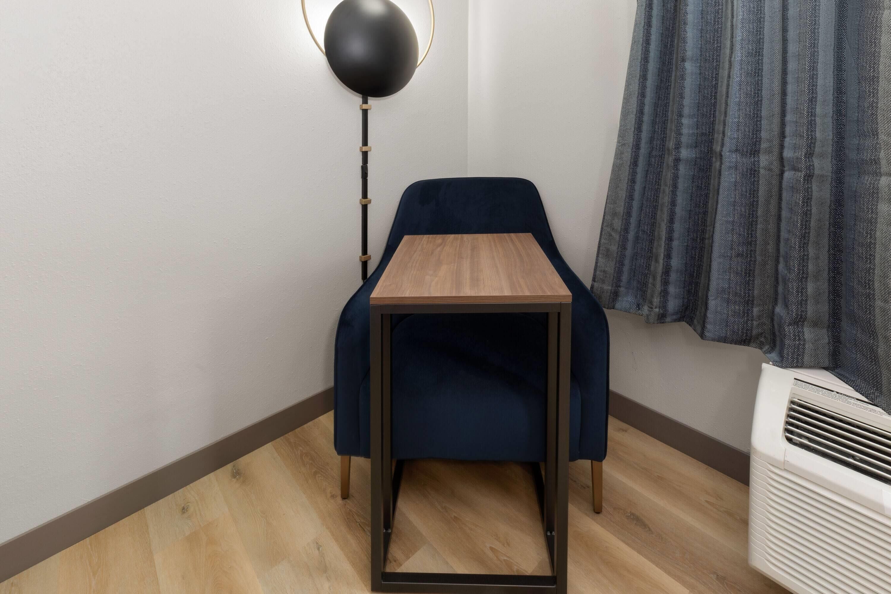 Ein Eckzimmer mit einem kleinen Tisch, einem Stuhl, einer Stehlampe und einer Klimaanlage.