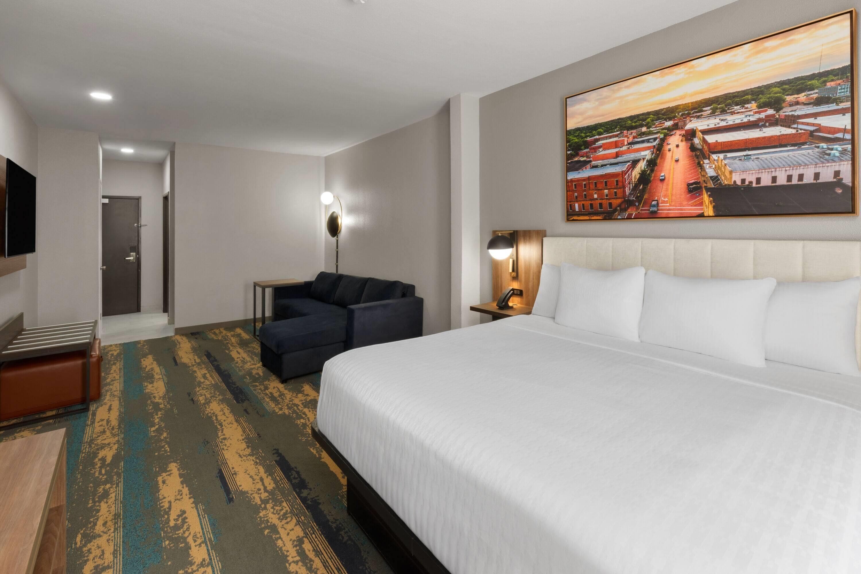 Una habitación de hotel con una cama grande, un sofá, un escritorio, un televisor y un cuadro en la pared.