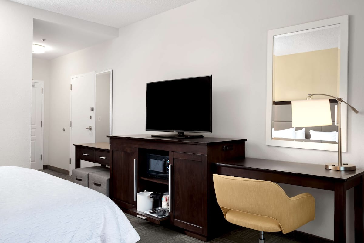 Habitación de hotel con una cama, un televisor sobre un mueble de madera, un espejo y una silla.