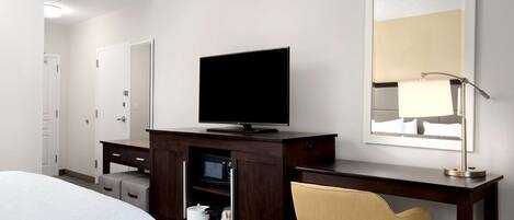 A hotel room with a bed, a TV on a wooden cabinet, a mirror, and a chair.