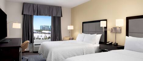 A hotel room with two beds, a desk, a chair, a TV, and a window with curtains.