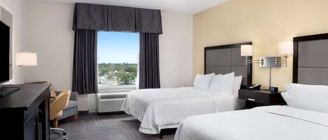 A hotel room with two beds, a desk, a chair, a TV, and a window with curtains.