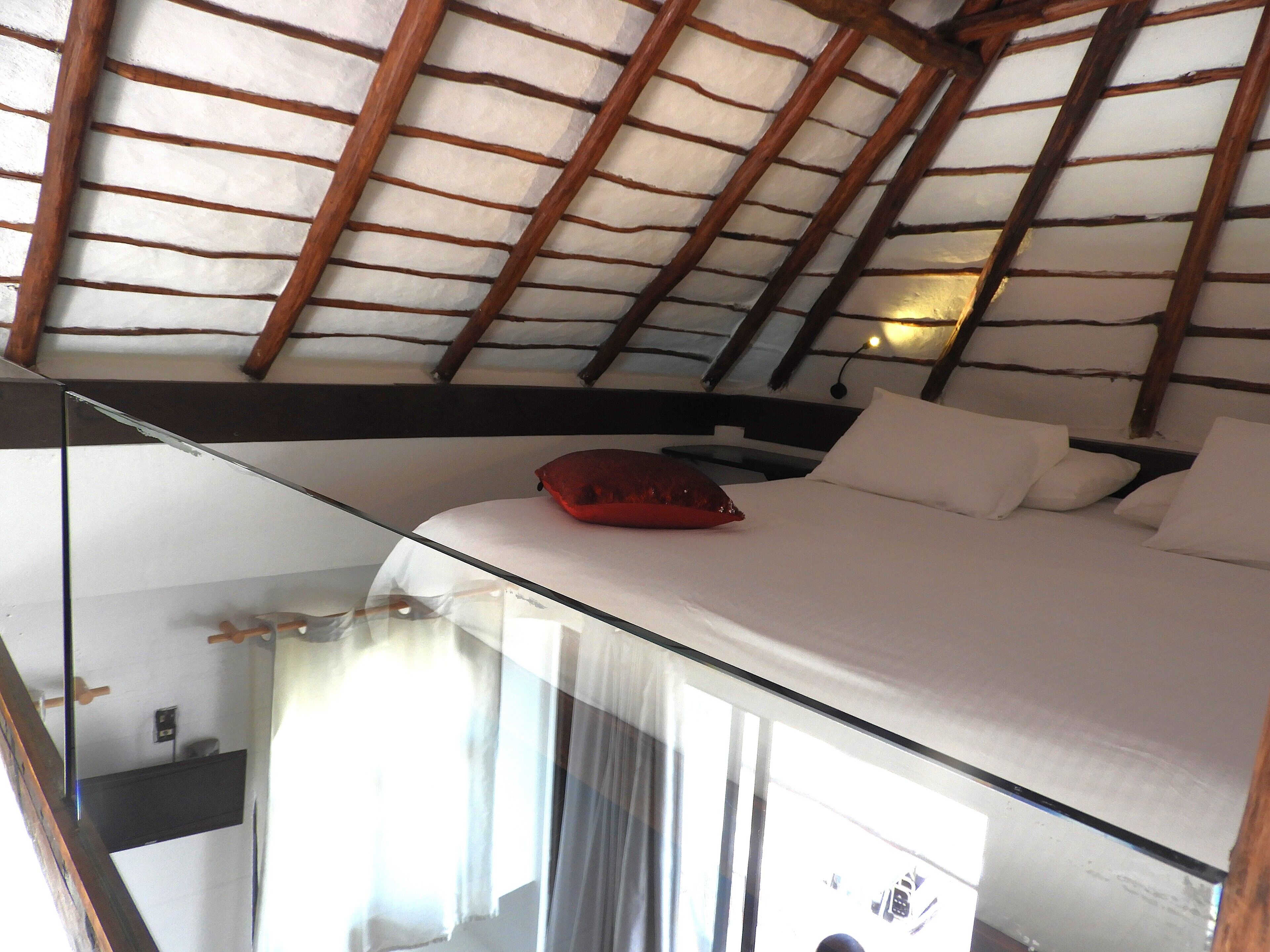 Une chambre avec un plafond en pente, un lit avec une literie blanche et un oreiller rouge.
