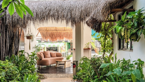 A cozy lounge area with a sofa and coffee table, surrounded by lush tropical plants and a thatched roof. - Kinbe Hotel Boutique (Playa del Carmen)