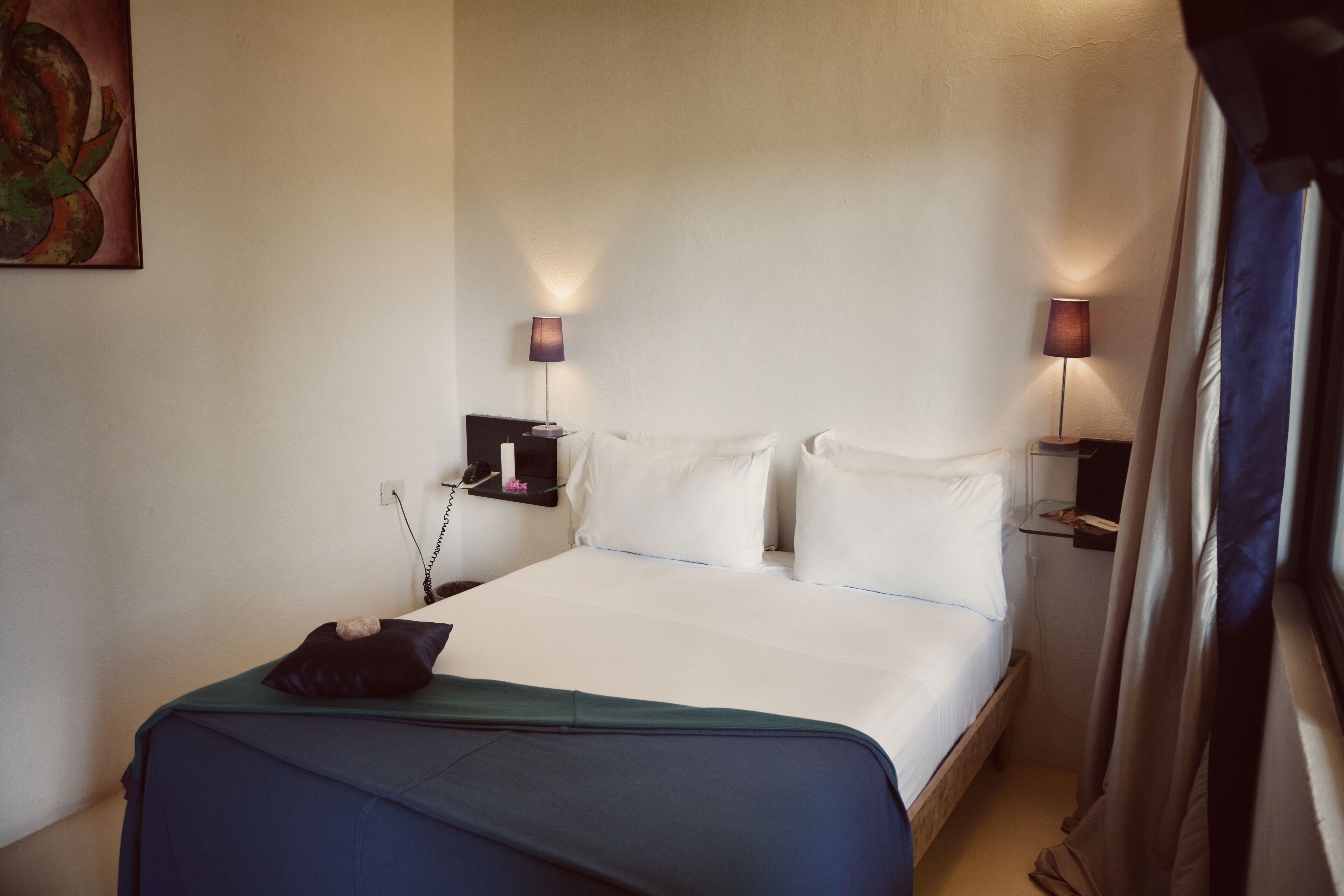A hotel room with a bed, bedside tables, lamps, and a painting on the wall.
