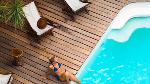 A poolside area with a wooden deck, lounge chairs, and a person sitting by the pool. - Kinbe Hotel Boutique (Playa del Carmen)