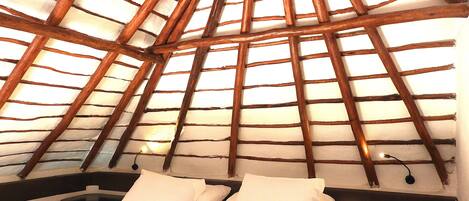 A room with a sloped wooden ceiling, a bed with white bedding, and a red pillow.