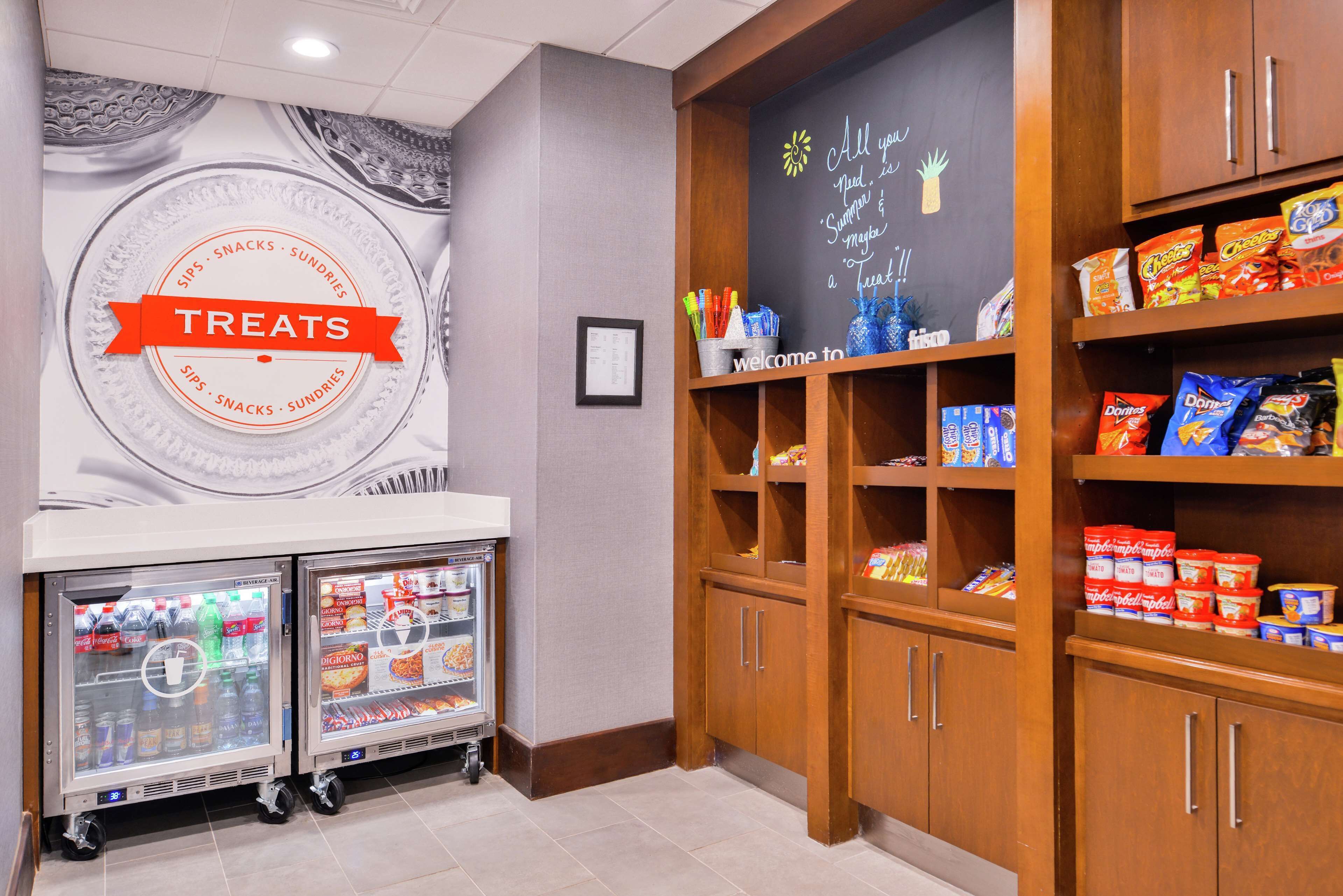 A snack bar area with a 'Treats' sign, refrigerated drink dispensers, and shelves stocked with various snacks and condiments.