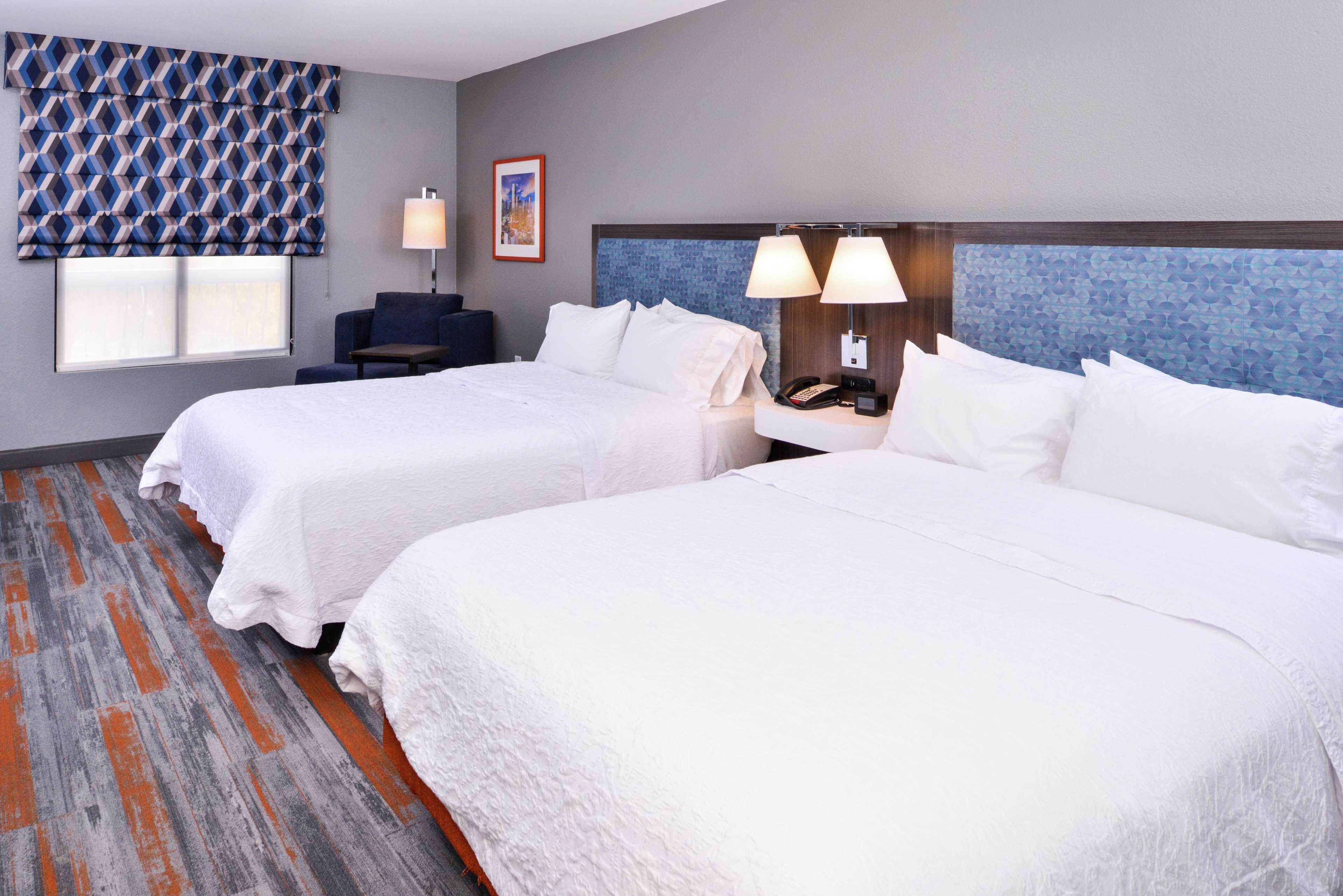 A hotel room with two beds, a desk, and a chair.