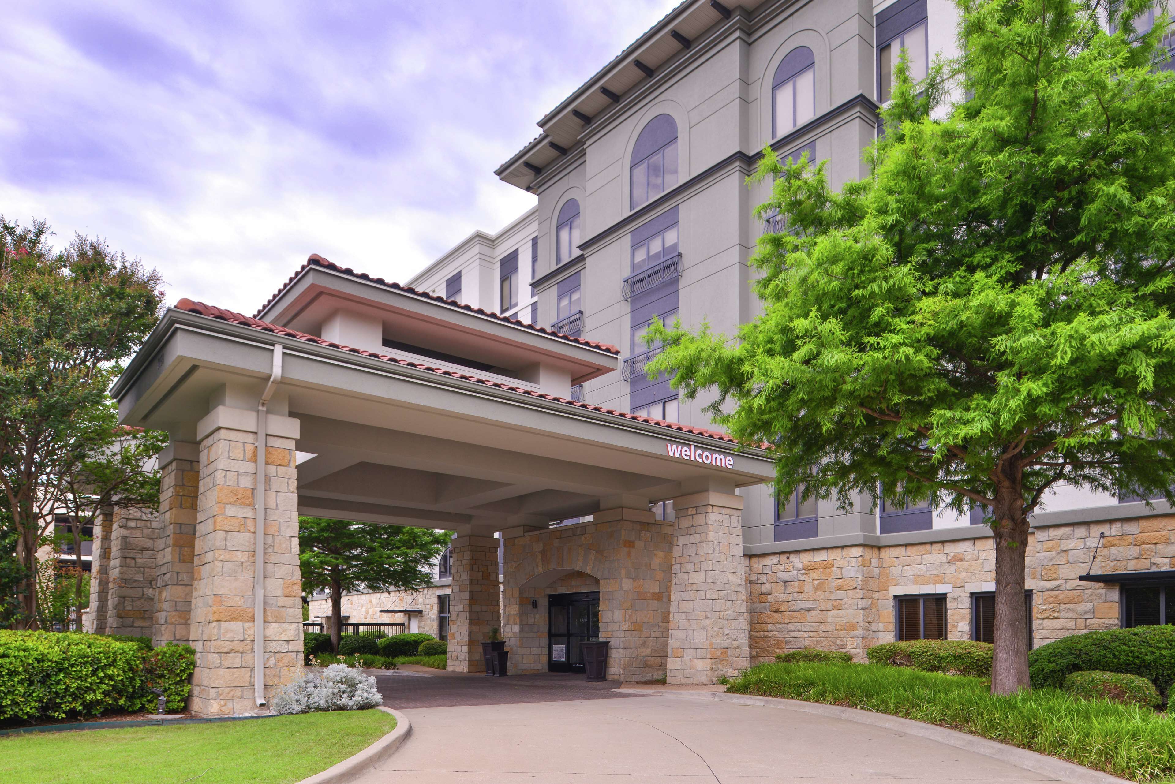 A hotel entrance with a stone facade, a covered walkway, and a sign that reads "welcome".