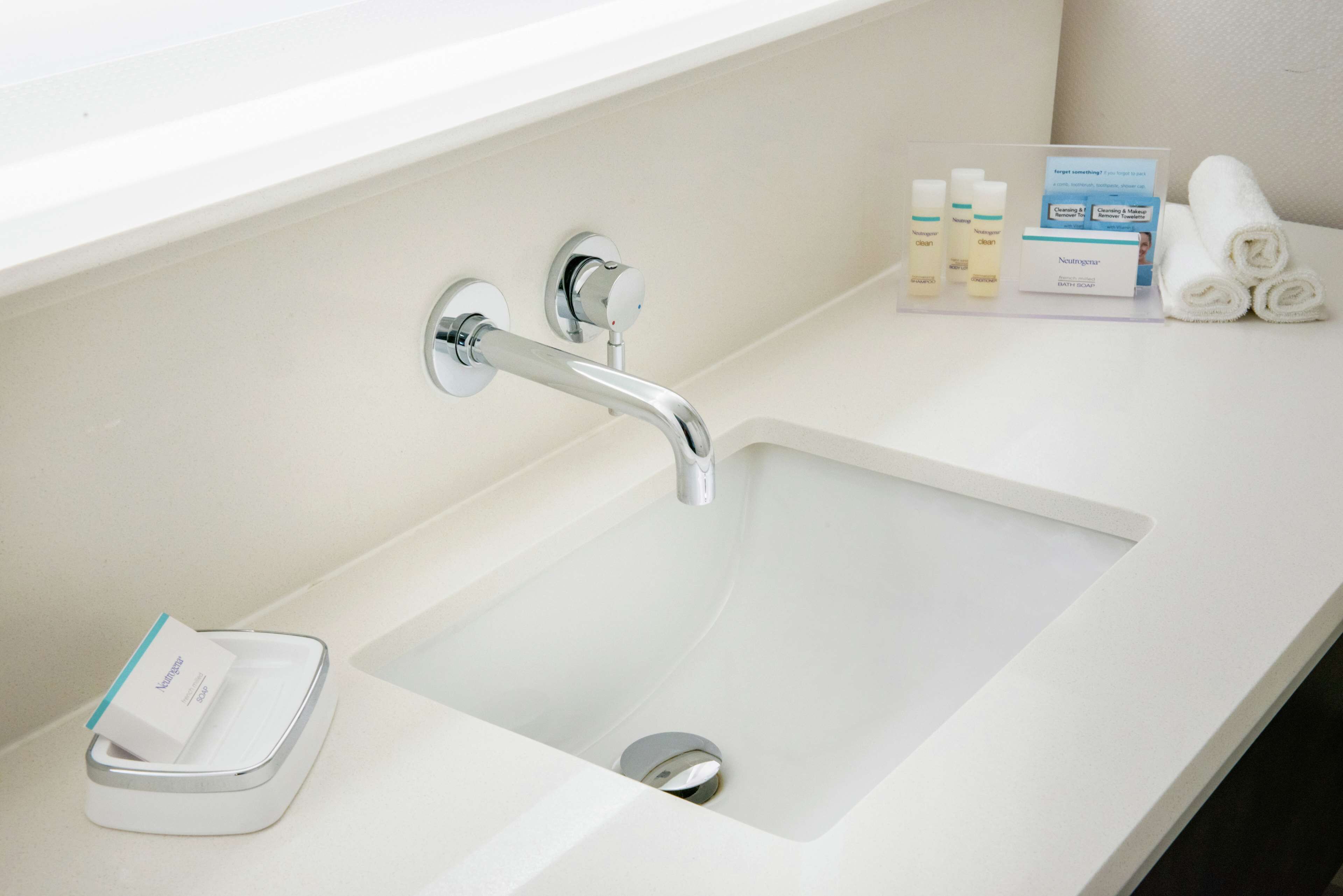 A modern bathroom with a white sink, chrome faucet, and a soap dish.
