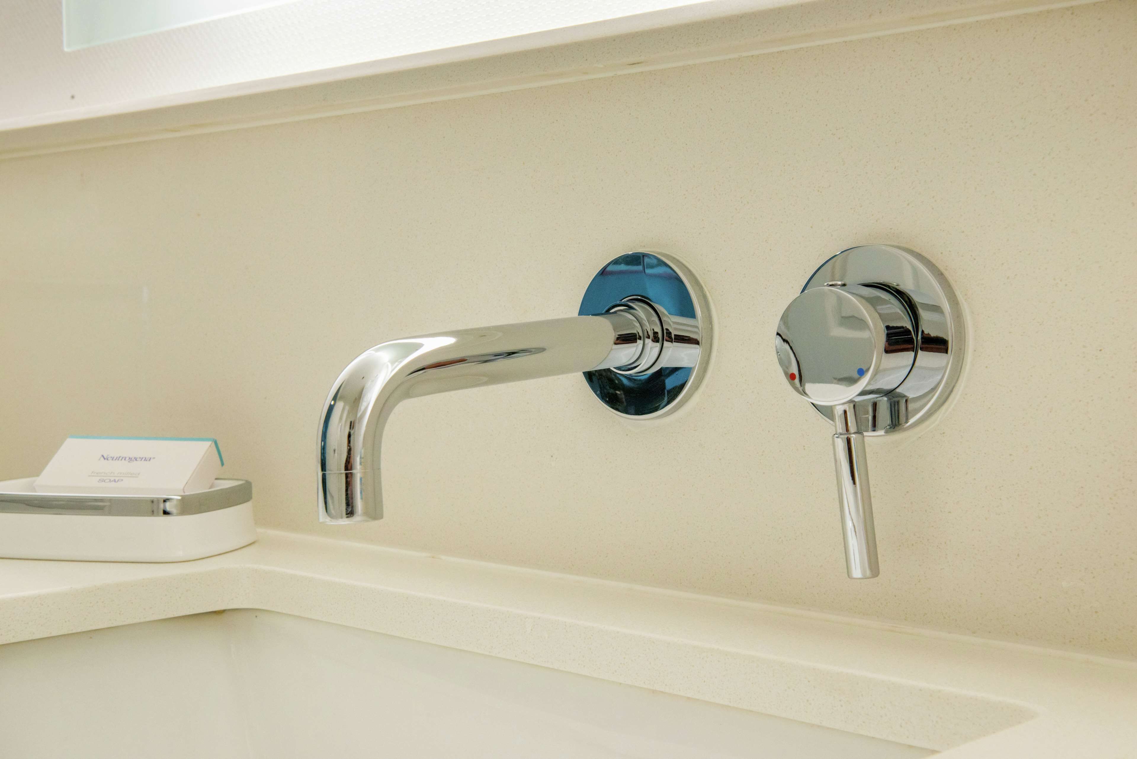 A modern bathroom with a white sink and two chrome faucets.