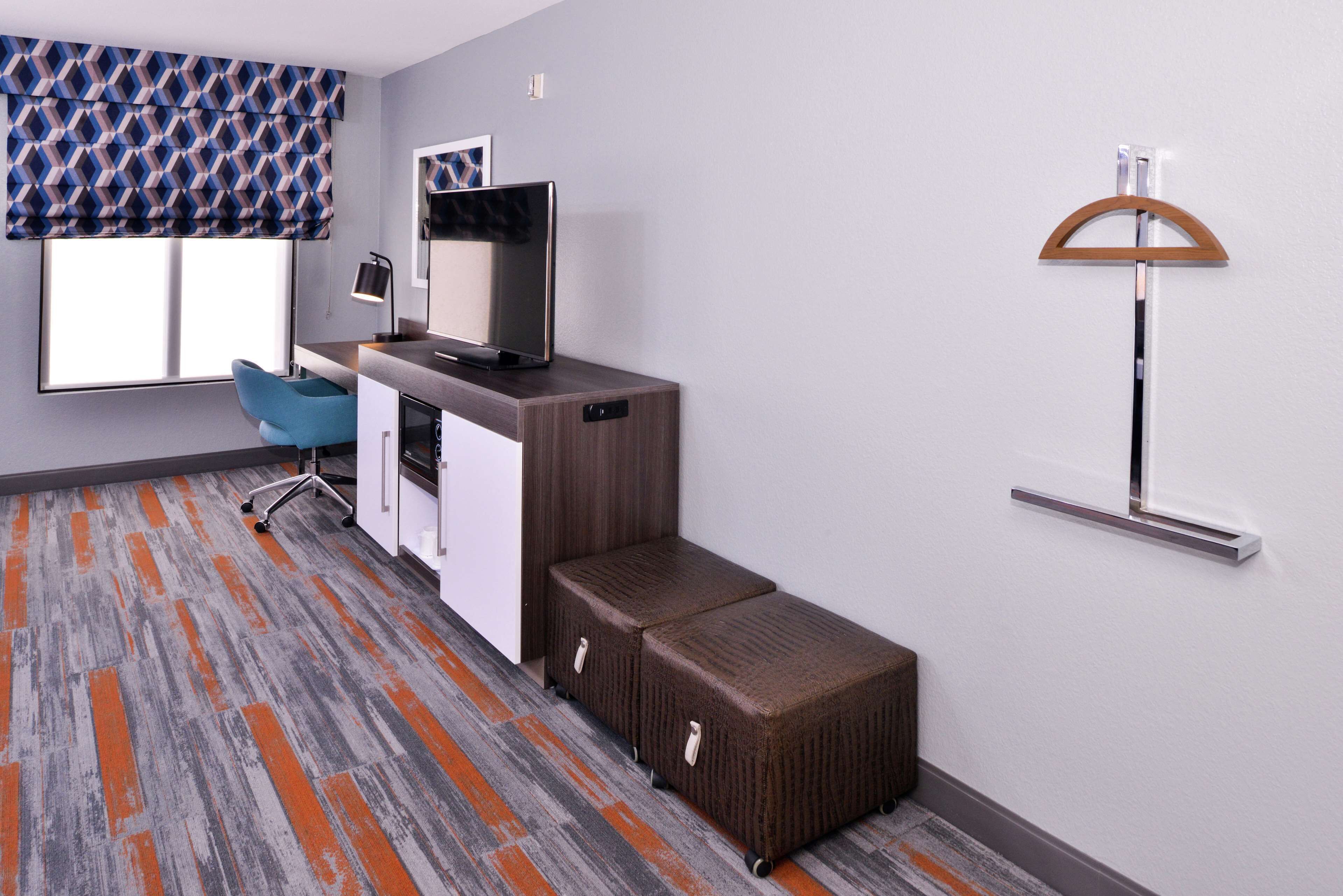 A modern hotel room with a desk, chair, and a large window with a patterned blind.