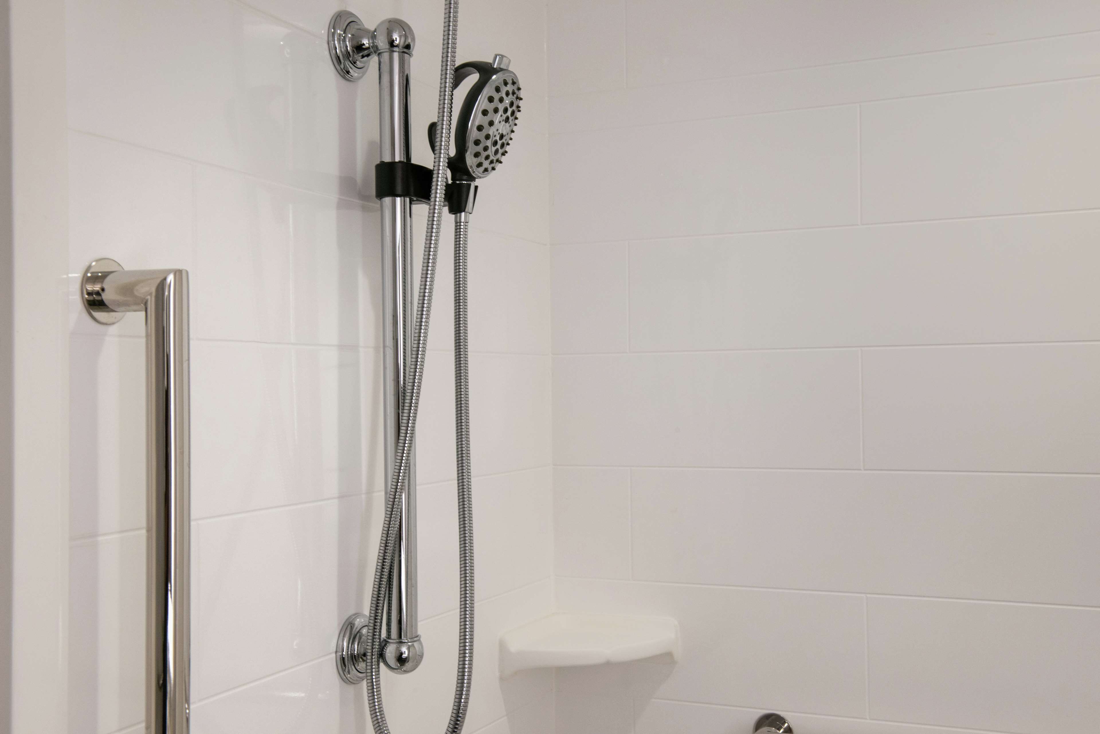 Une douche moderne dotée d’un pommeau de douche à main et d’un pommeau de douche fixe, de robinetterie chromée et d’un mur recouvert de carreaux blancs.