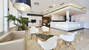 A modern reception area with a reception desk, seating area, and a large potted plant. - Hotel Globales Cala´n Bosch (Ciutadella de Menorca)