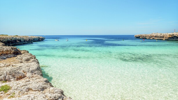 A coastal scene with clear turquoise waters, rocky cliffs, and a lighthouse. - Hotel Globales Cala´n Bosch (Ciutadella de Menorca)