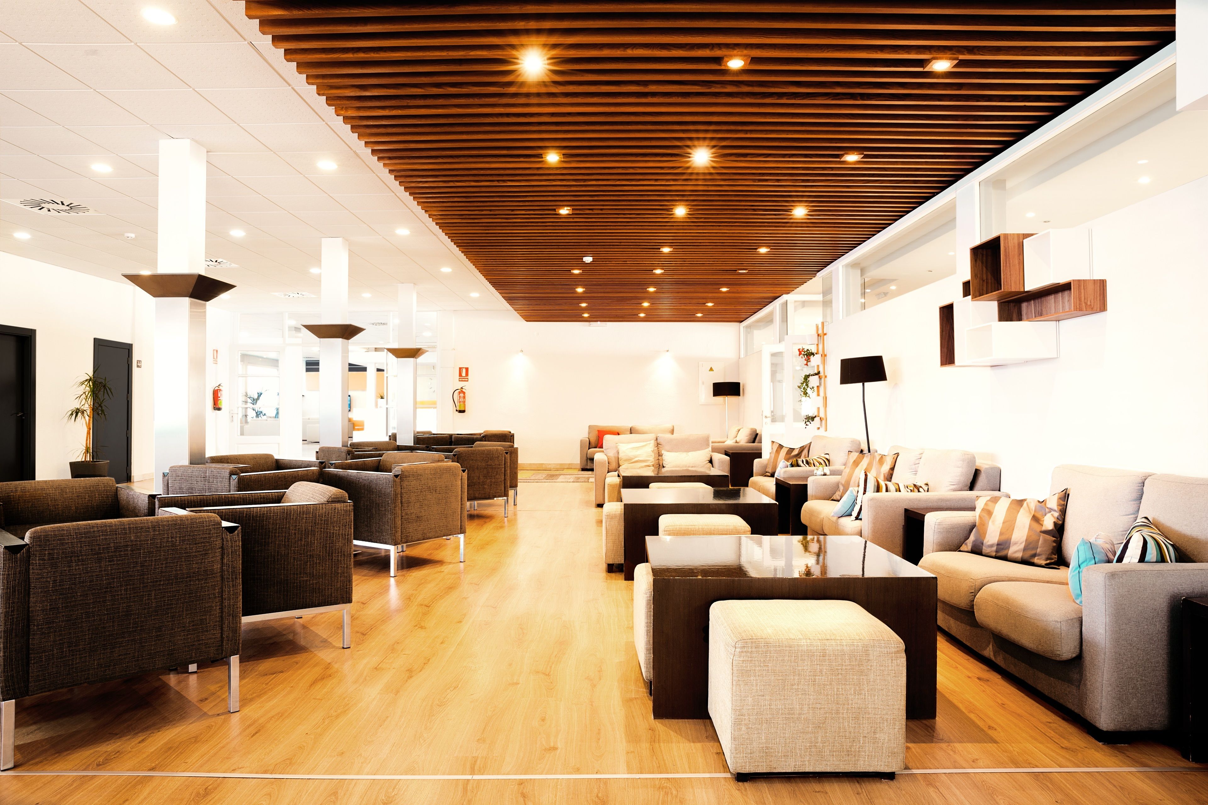 Een moderne lobby met een houten plafond, diverse zithoeken en een groot raam.