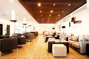 Una hall moderna con soffitto in legno, diverse zone relax e un'ampia finestra.
