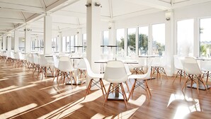 A spacious indoor area with rows of white chairs and tables, large windows, and a high ceiling. - Hotel Globales Cala´n Bosch (Ciutadella de Menorca)