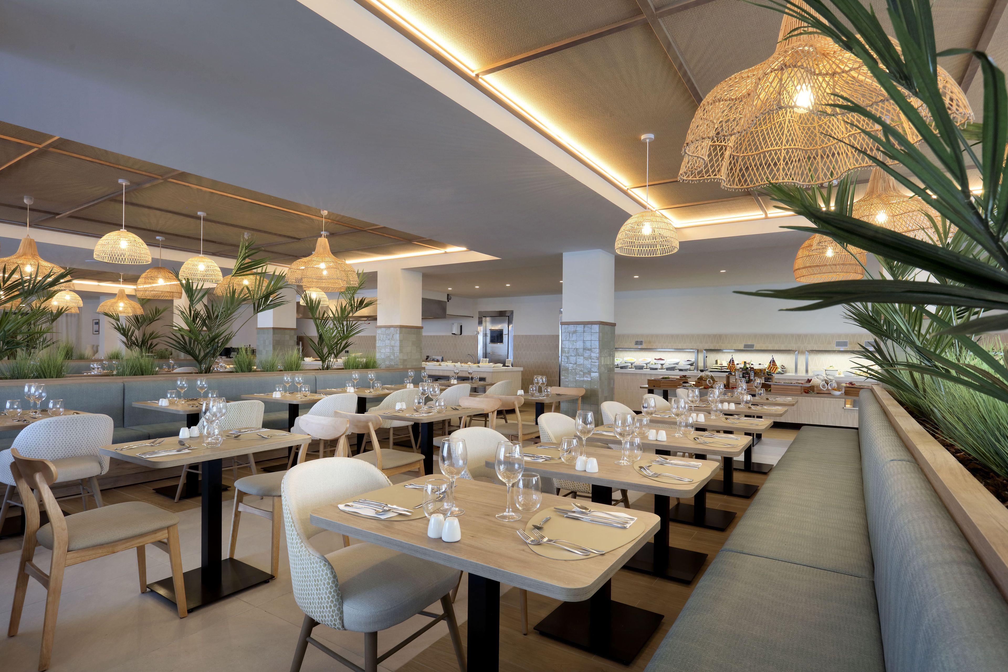 Restaurante com várias mesas, cadeiras e luminárias de rattan pendentes.
