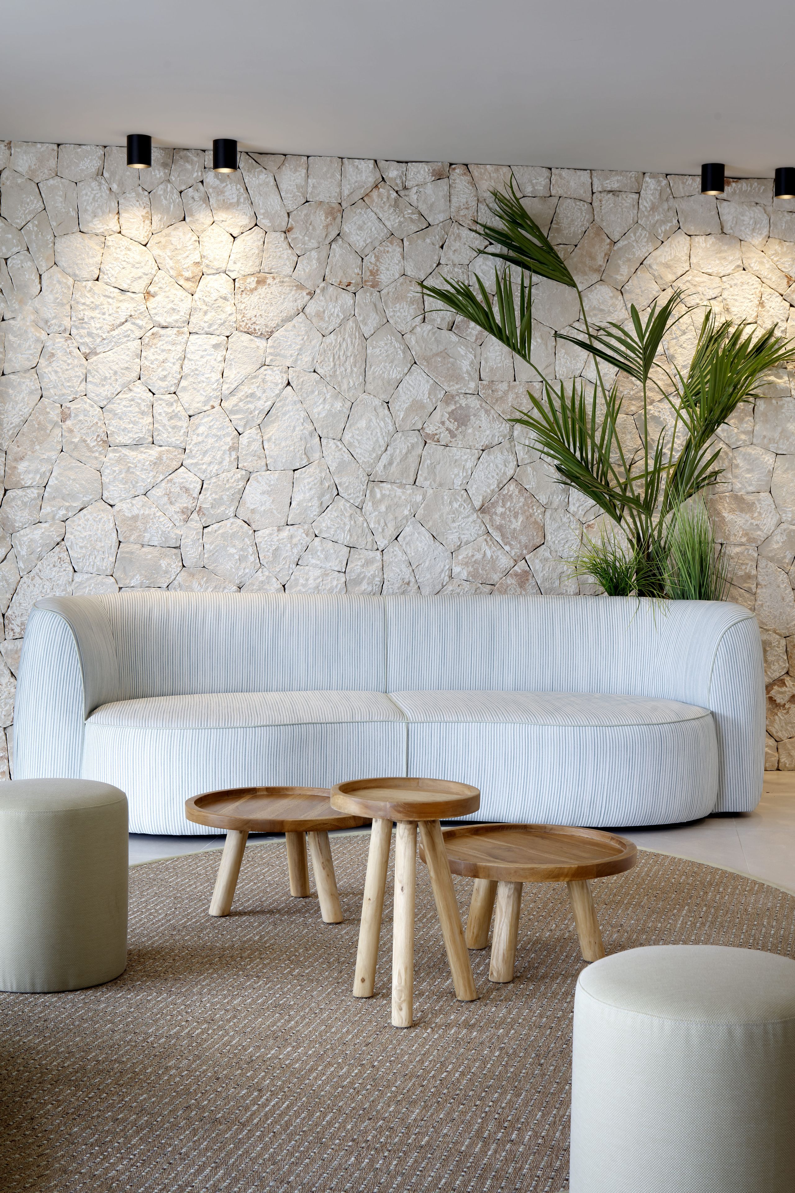 Uma sala de estar moderna com parede de pedra, sofá listrado, mesas de madeira e uma planta em vaso.