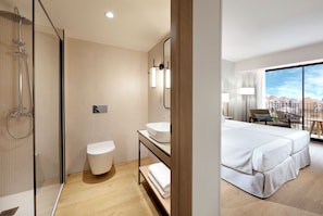 Een moderne hotelkamer met douche, toilet, wastafel en een bed met uitzicht.