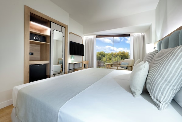Een hotelkamer met een groot bed, een bureau, een stoel, een televisie en een balkon met uitzicht op bomen.