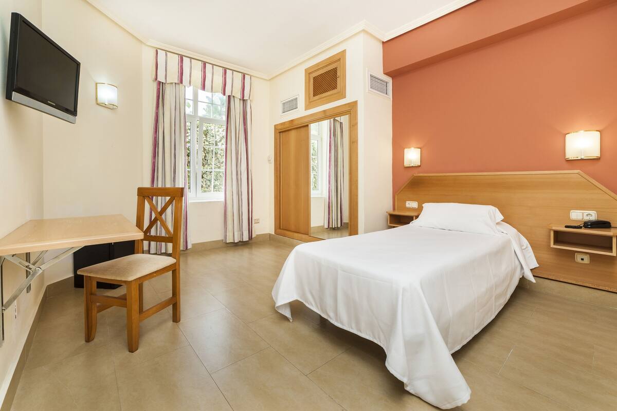 Ein Hotelzimmer mit Bett, Schreibtisch, Stuhl, Fernseher und zwei Wandlampen.