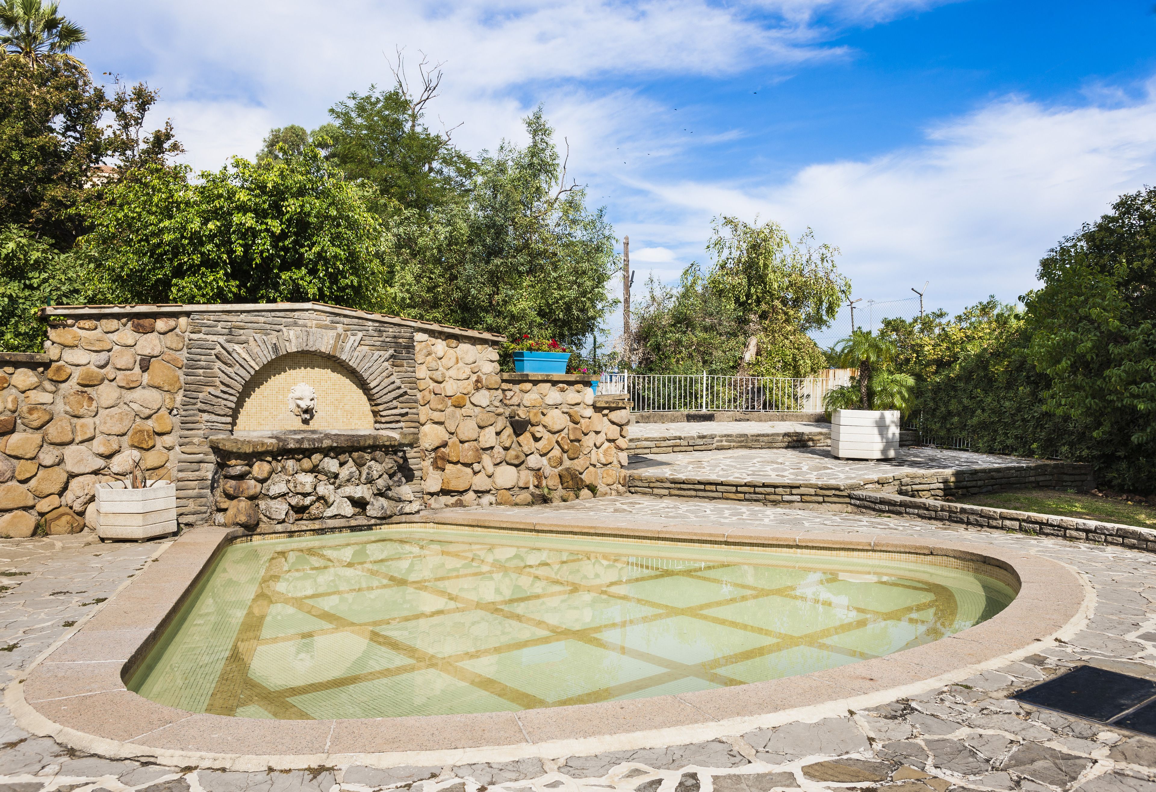 A stone pool with a stone wall and a small fountain, surrounded by greenery.