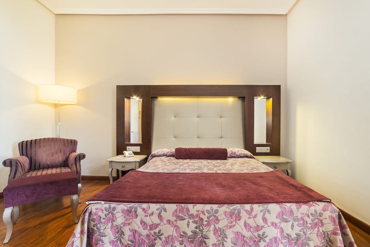 Ein Hotelzimmer mit einem großen Bett, einem Sessel, einem Nachttisch und einer Lampe.