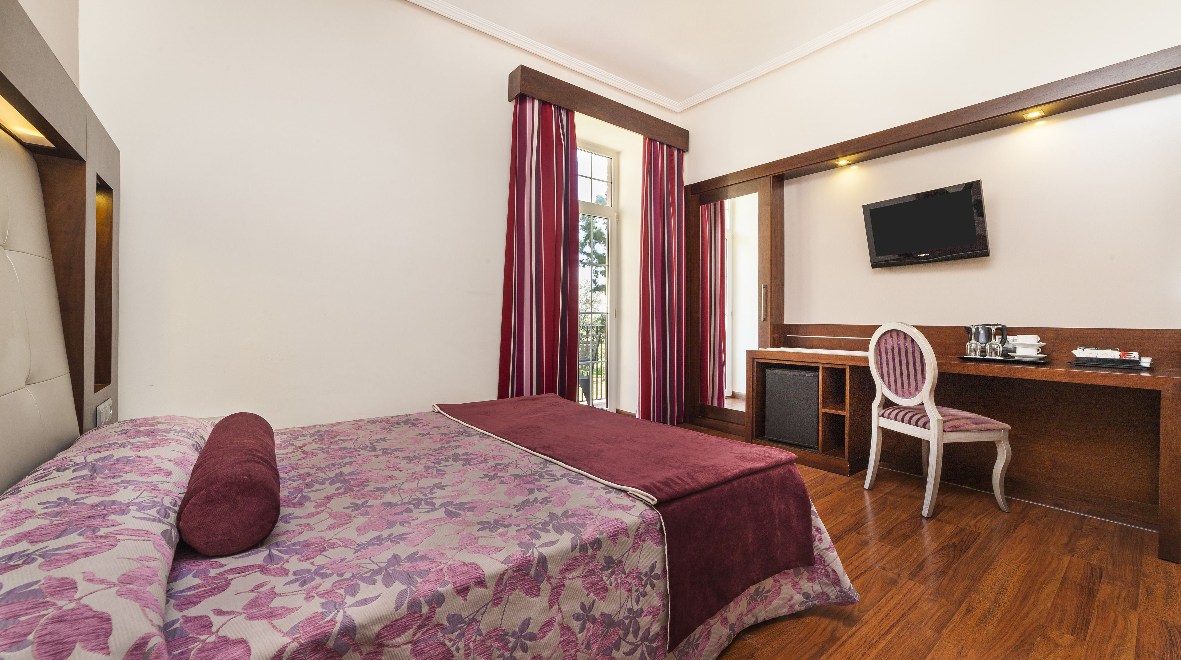 Een hotelkamer met een bed, bureau, stoel, televisie en een kleine koelkast.